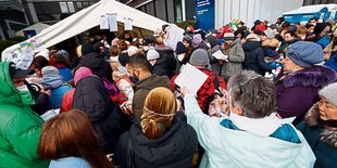 Menschen in Winterkleidung stehen gedrängt vor einem Zelt