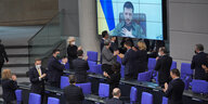 Der ukrainische Präsident Selenski ist auf einer Videoleinwand im Bundestag zu sehen, die Mitglieder der Bundesregierung applaudieren