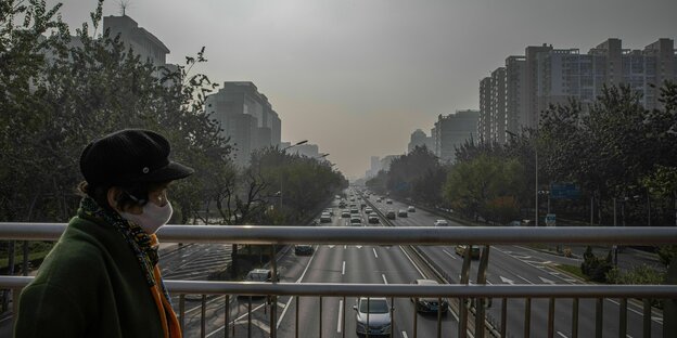 Eine Frau geht an einem verschmutzten Tag in Peking auf einer Brücke über eine Straße mit Autos,