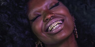 Das Porträt einer schwarzen Frau, die auf ihren Zähnen in goldenen Buchstaben "Equal Pay" stehen hat