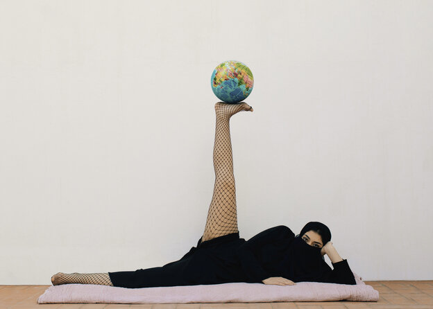 Eine Frau liegt seitlich auf dem Boden und balanciert auf einem Fuß eine Weltkugel