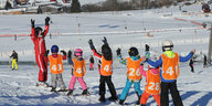 Kinder fahren in einer Reihe auf eine Skilehrerin zu