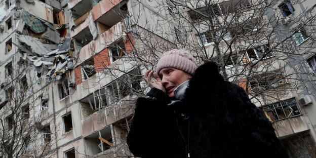 Eine erschütterte Frau weint vor einem zerstörten Gebäude