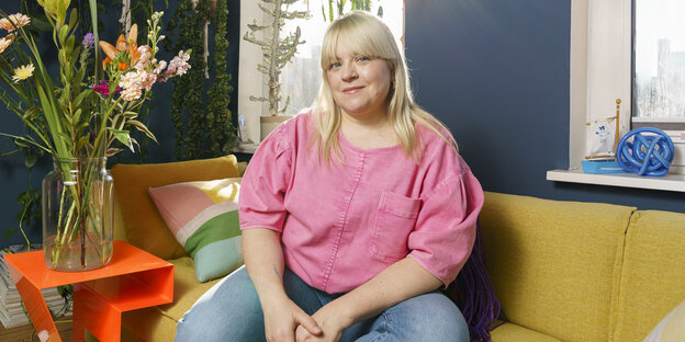 Melodie Michelberger sitzt mit einem rosa Oberteil auf einem gelben Sofa