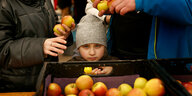 Ein Kind schaut über eine Kiste mit Äpfeln, während ihre Eltern Lebensmittel an der Essenausgabe für Flüchtlinge holen in der "Welcome Hall Land Berlin"