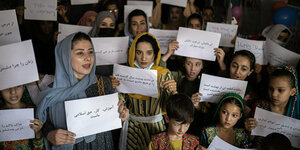 Eine Gruppe Frauen und Mädchen hält in arabischen Lettern beschriftete A4-Blätter hoch.