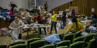 Frauen stehen in einem Höhrsaal und sortieren Kleidung