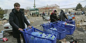Meschen auf einem vermüllten und herabgekommenen Platz schieben Einkaufswagen, die mit Plastikwasserflaschen gefüllt sind