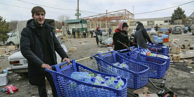 Meschen auf einem vermüllten und herabgekommenen Platz schieben Einkaufswagen, die mit Plastikwasserflaschen gefüllt sind