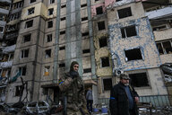 Ein Soldat in Tarnkleidung raucht eine Zigarette und geht an einem zerstörtem Gebäude vorbei