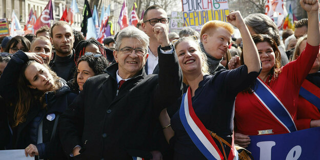 Jean-Luc Mélenchon trägt Mantel und Brille und reckt umringt von Menschen die Faust in die Luft