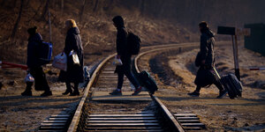 Eine Familie mit Koffern im Gegenlicht, sie überquert Bahngleise an der polnisch-ukrainischen Grenze.