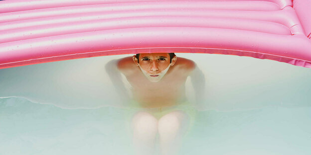 Ein Junge im Swimmingpool unter einer Luftmatratze