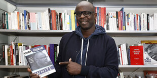 Lilian Thuram vor einem Bücherregal mit seinem Buch in der Hand