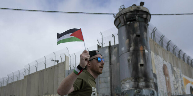 Ein Läufer mit einer palästinensischen Fahne vor einer Betonmauer.