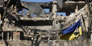 Eine zerrissene ukrainische Flagge vor einem zerstörten Haus