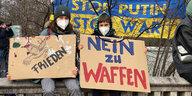 Zwei Menschen, die Papptafeln halten mit den Slogans "Frieden" und "Nein zu Waffen"