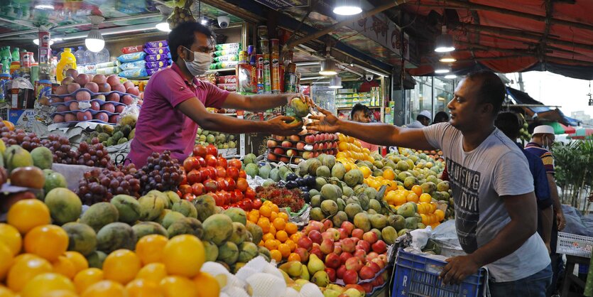 Zwei Personen an einem Obst- und Gemüsestand auf einem Markt.