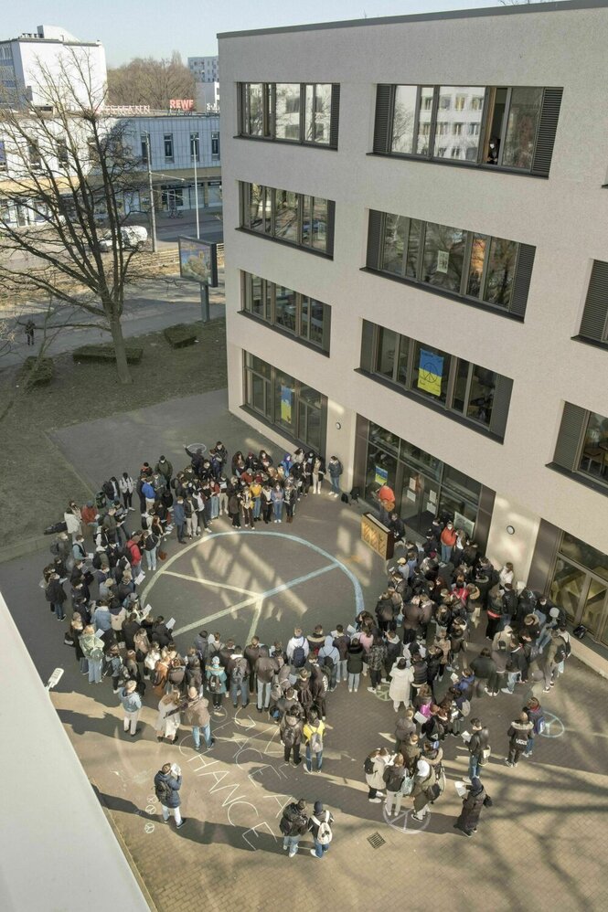 Schüler stehen um ein aufgemaltes Peace Zeichen im Schulhof herum