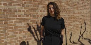 Luisa Neubauer - eine junge Frau in schwarzer Kleidung steht vor einer Ziegelwand
