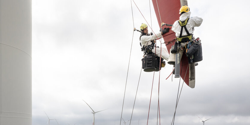 Zwei Industriekletterer hängen an Seilen an einem Windkraftrotor