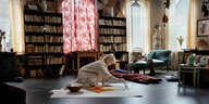 Eine blonde Frau sitzt auf em Boden in ihrem Atelier und malt