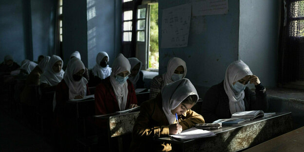 Mädchen mit weißen Kopftchern schreiben konzentriert an ihren Pulten im Klassenzimmer.