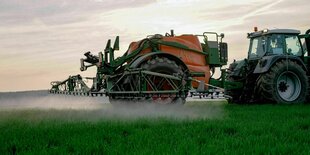 Sprühnebel von Plfanzenschutzmittel, das von einem Traktor auf ein Feld ausgebracht wird, im Gegenlicht