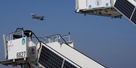 zwei Fluggastbrücken mit Solarzuellen, dazwischen ein Flugzeug am Himmel