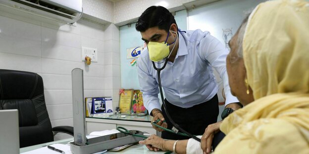 Ein Mann mit Schutzmaske misst bei einer Patientin den Blutdruck