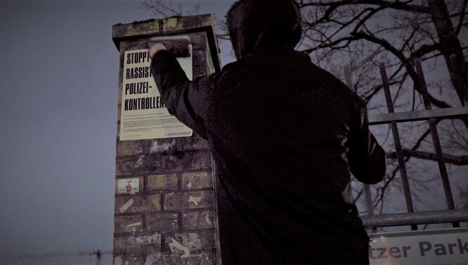 Eine Person klebt ein Plakat gegen rassistische Polizeikontrollen