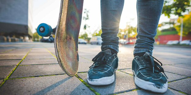 Eine Person mit Sneakers und Jeans und einem Skateboard