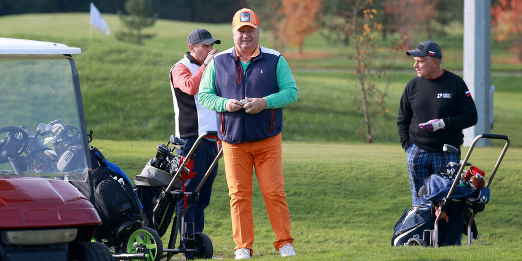 Ein älterer Man steht auf einem Golfplatz, daneben ein Golf-Car