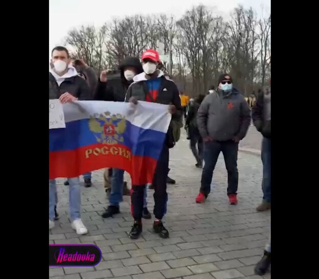Screenshot, Junge Männer mit FFP2 Masken halten eine russische Flagge in den Händen