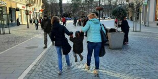 Zwei Frauen mit einem Kind in der Mitte, das sie hochfliegen lassen