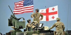Soldaten auf einem Panzer, im Hintergrund weht die Flagge Georgiens und der Vereinigten Staaten