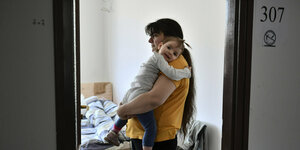 Eine Frau mit einem Kind auf dem Arm steht in einer Tür vor einem Bett