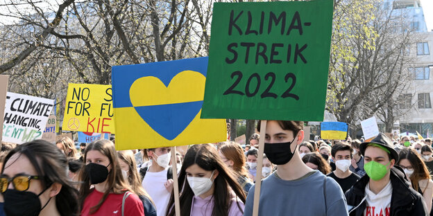 Junge Menschen auf Demo, im Vordergrund Demoschilder mit einem Herz in Ukraine-Farben und der Aufschrift "Klimastreik 2022"