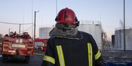 Feuerwehrperson von hinten. Im Hintergrund Industrietürme