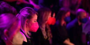 Junge Frau steht mit FFP2 Maske in einem Zuschauerraum, rötliches Licht