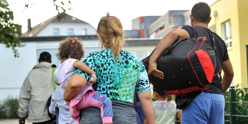 Eine Familie läuft mit Reisetaschen über einen Hof