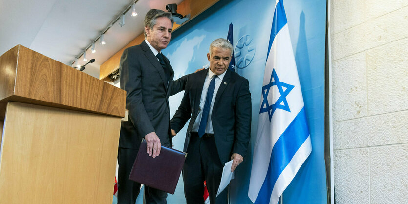 Antony Blinken und Yair Lapid tragen Anzüge und verlassen zusammen ein Podium