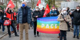 Vor dem russischen Generalkonsulat stehen Demonstrant*innen mit Flaggen der Partei Die Linke und einer Regenbogenflagge mit dem Wort "Pace" - also "Frieden"