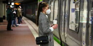 Eine Frau mit Kaffeebecher steht vor einer haltenden Bahn