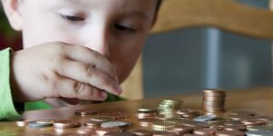 Eine kleiner Junge legt Geldmünzen auf einen Tisch