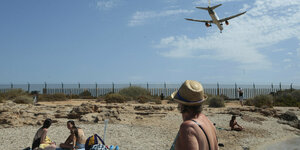 Ein Flugzeug fliegt über Strandurlauber:innen auf Mallorca