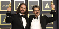 Alberto Mieglo und Leo Snachez posieren in schwarzen Fracks und Fliegen mit 2 Oscars