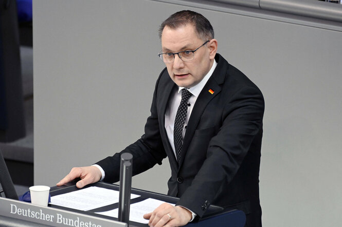 Ein Mann mit Deutschland-Flagge-Brosche am Jacket am Rednerpult des Bundestages