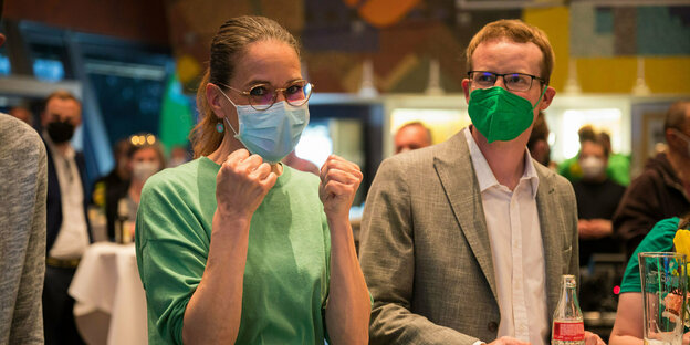 Uta Sullenberger trägt auf der Wahlparty der Grünen einen grünen Pullover und eine weiße Maske, beide Hände hält sie zu Fäusten hoch, die Daumen gedrückt.