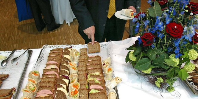 Buffet und ein Herr mit Anzug, daneben ein Blumengesteck